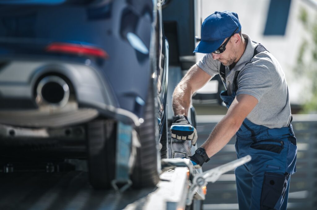 towing company worker securing vehicle on the truck platform